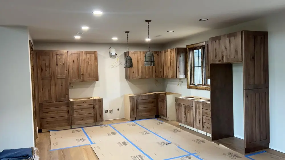 Kitchen cabinet run being installed, with floor protection down over the finished floor